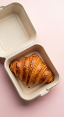 Golden croissant in open eco friendly takeout container on pink background