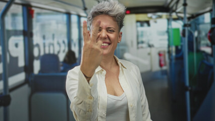 Woman with short hair clenches her fists and grins widely in a brightly lit colorful bus interior; triumph.