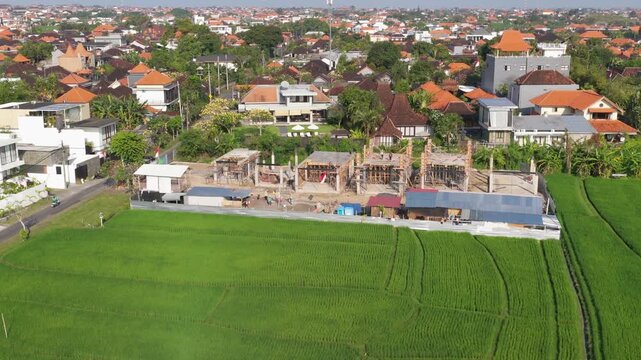 Aerial view of construction site emerging among green rice fields and surrounding residential neighborhood in Bali