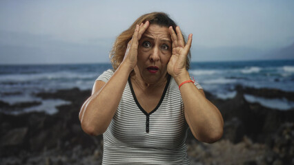 Woman hispanic middle age wearing striped shirt holds up crossed palms shielding face in studio setting with soft focus lighting; rejection defiance resistance.