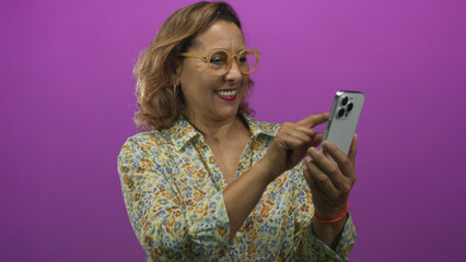 Woman holding smartphone with finger pointing at screen in purple studio wearing floral blouse;...