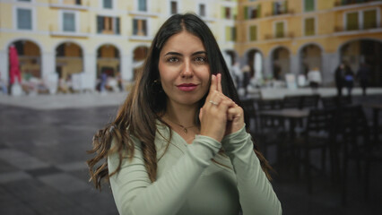 Fototapeta premium Young woman makes finger gun gesture with hands on historic street wearing a green shirt; fun pretend play.