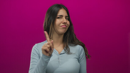 Fototapeta premium Young hispanic woman pointing her index finger with a dismissive gesture in an isolated pink studio setting; denial.