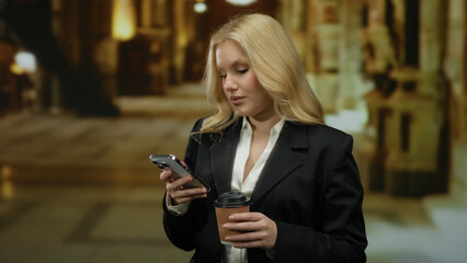 Woman browsing smartphone in elegant museum setting with coffee in hand, surrounded by artful atmosphere, showcasing modern lifestyle and youthful charm in sophisticated attire.
