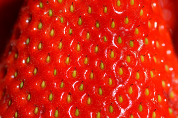 An extreme close up shot of a ripe red strawberry showing detailed texture and seeds under bright lighting