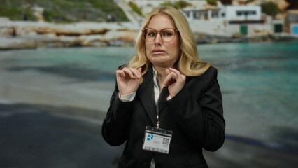Woman in glasses at beach with id badge displays disgusted expression, blonde hair flowing,...