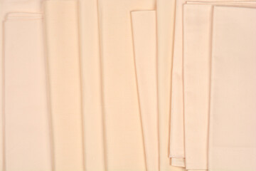 A top view of several folded light beige cotton tablecloths with a subtle dotted pattern stacked neatly on top of each other