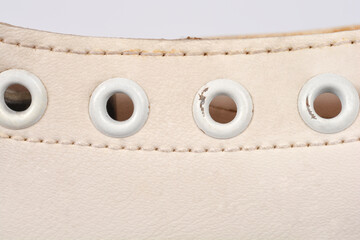 A macro view of white leather on a figure skate showing four metal eyelets for laces and detailed horizontal stitching on a neutral background