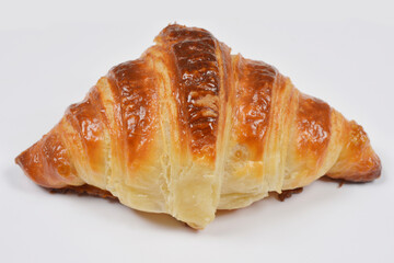 A close up shot of a single freshly baked golden brown croissant with a flaky crust isolated on a plain white background
