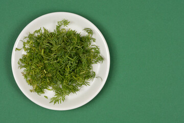 A white ceramic plate filled with freshly chopped green dill herb placed on a solid green surface with copy space on the right side
