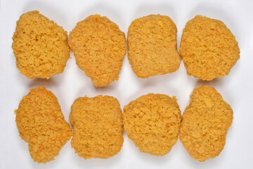 Eight breaded vegan chicken nuggets are neatly arranged in two rows on a plain white background after being removed from their packaging