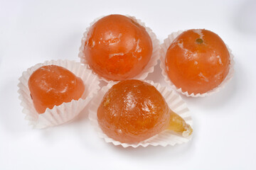 A selection of whole candied fruits including a pear apricot fig and clementines each with a shiny sugar glaze resting in white paper liners on a plain white surface