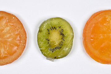 A top down view of three colorful candied fruit slices including green kiwi and orange arranged in a row on a plain white surface