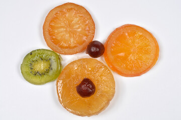 A collection of colorful candied fruit slices including orange, kiwi and pineapple with cherries on a plain white background