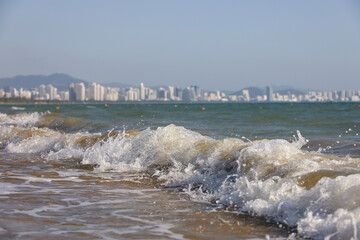 Sea sandy beach with surf waves on city buildings background. Background for travel and vacation