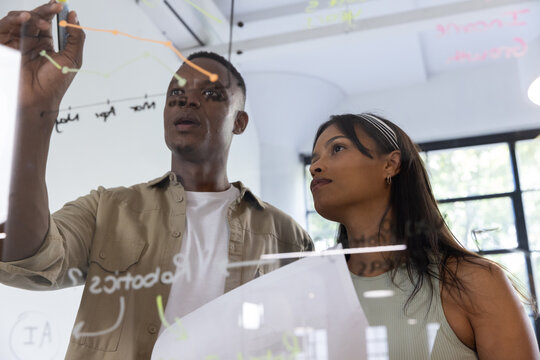 Diverse coworkers writing data on glass whiteboard, reviewing documents in office meeting room - Powered by Adobe