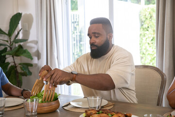 African American father and adult son sitting at dining table tossing salad with wooden servers