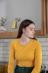 Woman leaning against countertop in kitchen featuring gray tile backsplash, pasta jars, brass lamp