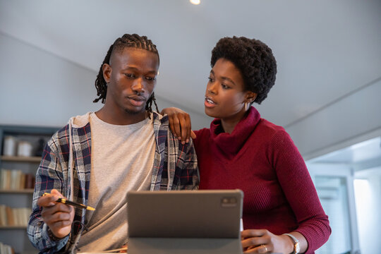 African american couple leaning over tablet and using stylus at home office table by bookshelf - Powered by Adobe