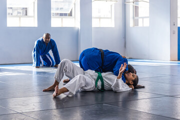 Diverse teenage students grappling on dojo mats in gis and african american instructor observing