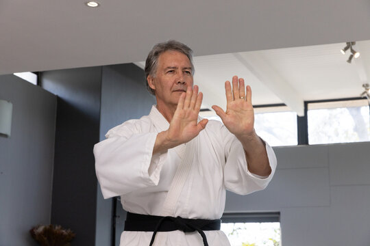 Senior male performing blocking technique in arts studio wearing karate gi and black belt