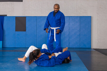 African american instructor guiding teenage female students grappling in gi on mats in dojo