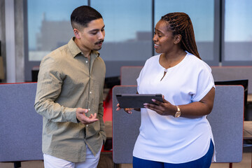 Diverse coworkers collaborating on digital tablet at office near partitioned desks, dividers