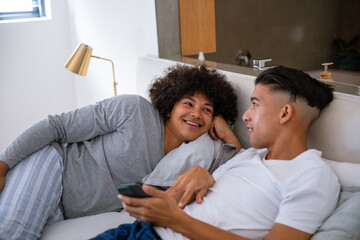 Diverse male friends lounging on sofa in home living area with striped pillow and smartphone