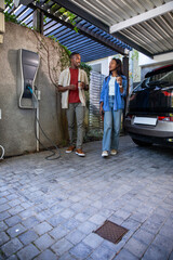 African American couple walking under carport holding coffee cups near EV charging station