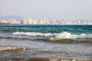 Scenic view to sea sandy beach with surf waves on city buildings background. Background for travel and vacation