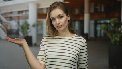 Fototapeta premium Woman holds open hand palm facing upward in spacious modern building; curiosity inquiry uncertainty question.