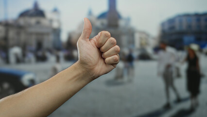 Hand with thumbs up gesture by man in vatican city san pedro square outdoor setting with blurred background.