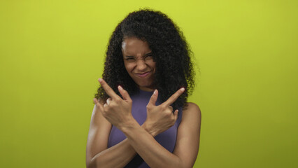 Young woman with curly hair and raised arms shows rock horns gesture in a yellow studio setting  fun vibe. © Krakenimages.com