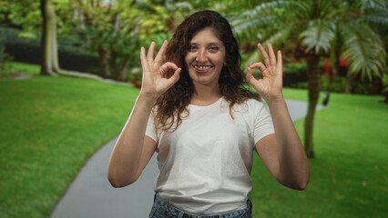 Woman smiling and making ok sign with both hands on a park path wearing tshirt; approval joy support.
