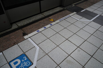 Waiting line sign and bicycle parking symbol on the floor of a subway platform.
