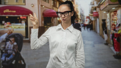 Fototapeta premium Woman wearing glasses, fingers poised to snap in a street market with white shirt visible; playful attitude.