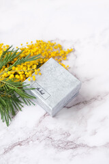 fluffy yellow mimosa flowers and gift box on marble background close up. spring season. festive composition. romantic gift for women, girl. copy space. template for design