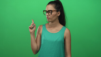 Woman points index finger toward camera in studio against vivid green background; disapproval firm...