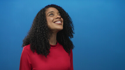 Woman smiling with white teeth and curly hair, head turned left in blue studio setting; joy...