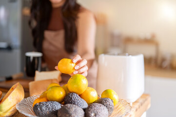 Close up of woman with coffee mug holding orange aside toaster standing at kitchen cooking counter.