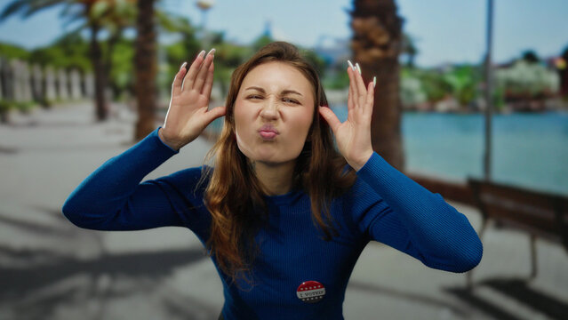 Woman making funny face with vote badge outdoors on beach promenade showcasing civic engagement and youthful expression.