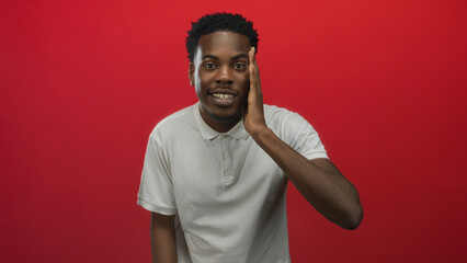 Young african american man touches cheek with hand while leaning forward wearing white polo shirt...