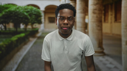 Fototapeta premium Man in white polo shirt with glasses gestures with raised hand in building; confidence focus optimism empowerment.