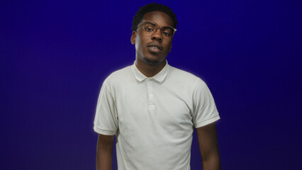 Man face smiling in studio under vibrant blue backdrop with casual white polo shirt; confidence ease.