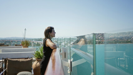 Naklejka premium Woman leaning on glass rail with bare forearm resting on cruise ship deck railing, smiling toward sea and distant shore; serenity travel.