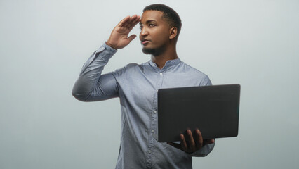 Man holding laptop, hand to forehead shielding eyes in studio while looking at screen and adjusting posture; relief focus.