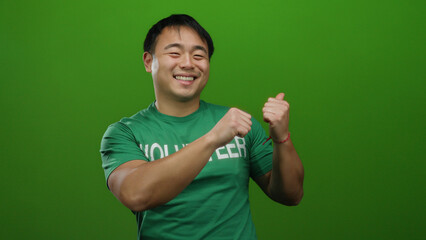 Fototapeta premium Young man in volunteer shirt smiles over green background, expressing positivity and energy.