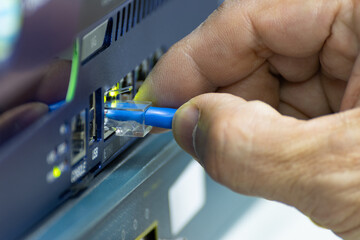 Close-up of a hand plugging a blue ethernet cable into a network switch or router. Concept data connection, internet technology, and IT infrastructure.