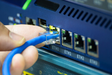 Close-up of a hand plugging a blue ethernet cable into a network switch or router. Concept data connection, internet technology, and IT infrastructure.