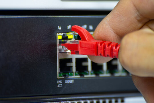 Close-up of a hand plugging a red ethernet cable into a network switch or router. Concept of data connection, internet technology, and IT infrastructure.